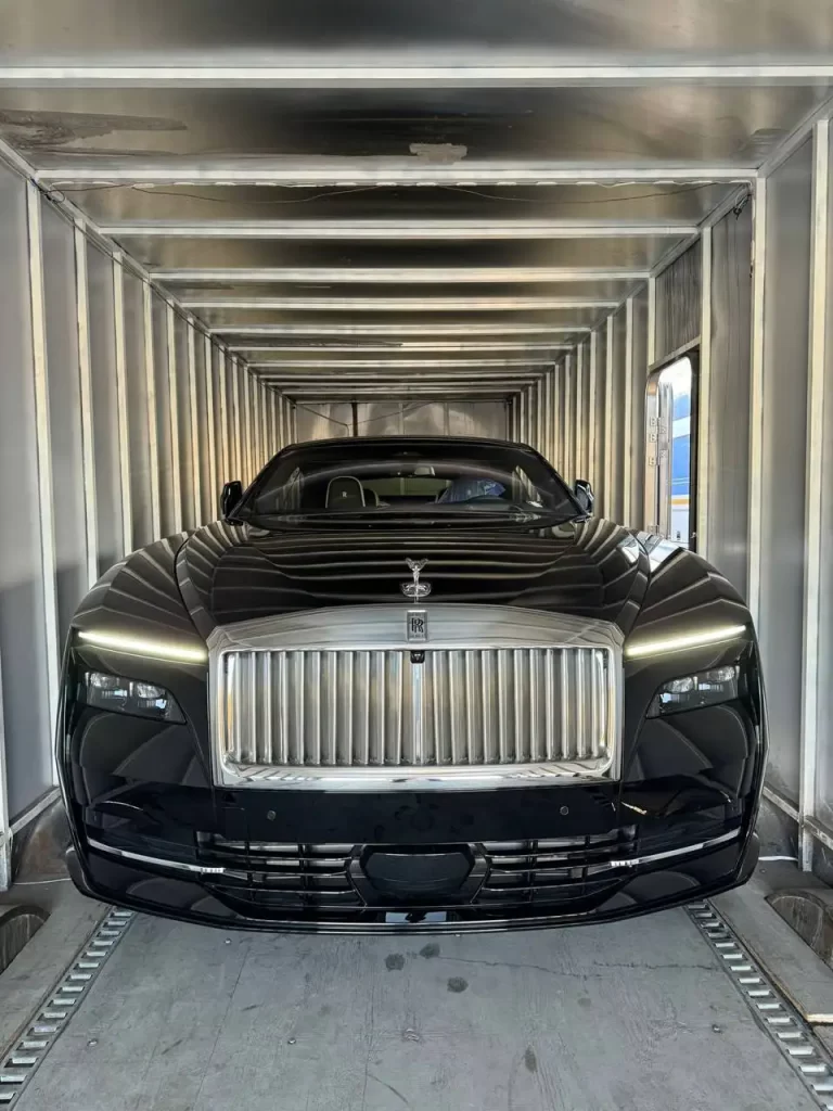 A sleek black Rolls-Royce is securely placed inside a well-lit car trailer.